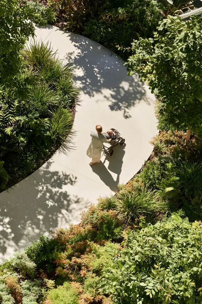 Mother pushing a stroller along a shaded clinic garden path